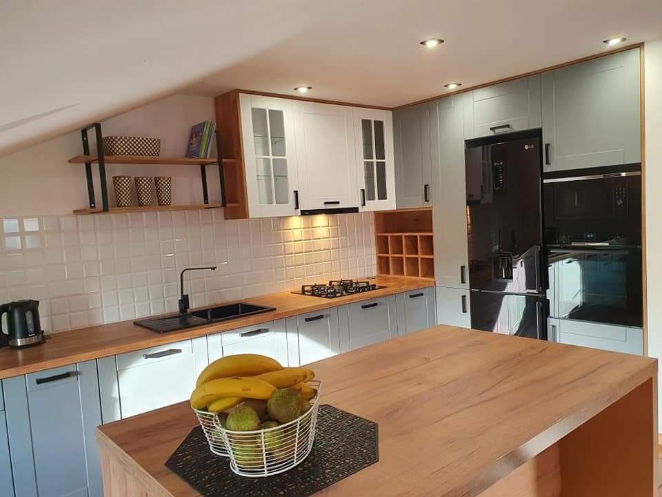 Nowoczesna kuchnia w Złoczewie z szarymi i białymi szafkami, drewnianym blatem i wyspą, czarnym sprzętem AGD i półkami na ścianie ze skośnym sufitem.