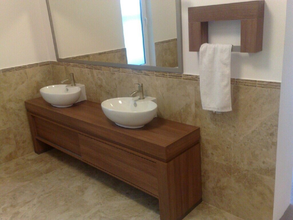 Łazienka z dwiema umywalkami nablatowymi na drewnianej szafce na wymiar, lustro w srebrnej ramie i drewniany uchwyt na ręcznik z białym ręcznikiem.