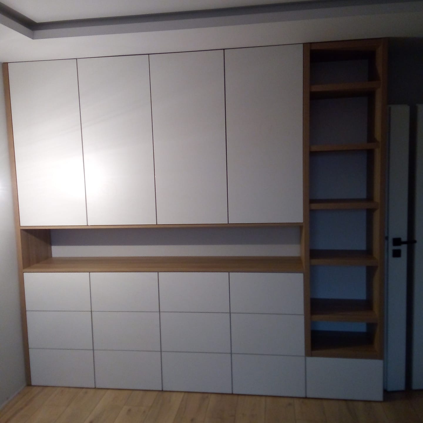 Biała szafa wnękowa z drewnianymi półkami i frontami, widok z bliska, oświetlenie mieszane.