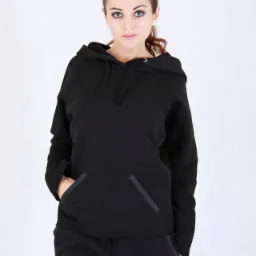 Kobieta prezentuje czarny dres z bluzą z kapturem i kieszeniami z ozdobnymi listwami, na białym tle, z widocznym logo marki.