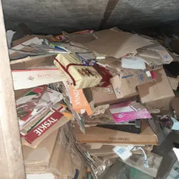 Stos kartonowych pudeł i opakowań w ciemnym pomieszczeniu, widoczne marki Tyskie, Brześć i ZinZinna.