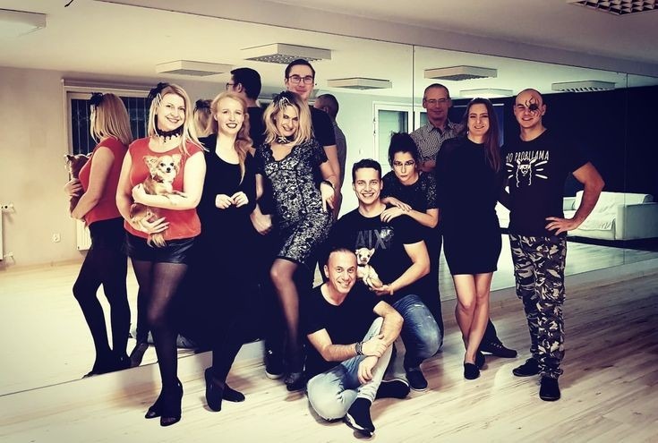 Grupa uśmiechniętych osób w różnym wieku pozuje w sali z lustrami, niektórzy trzymają małe psy.