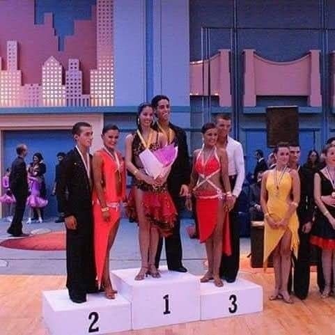 Tancerze w kolorowych strojach na podium po konkursie tańca, z dekoracją w tle przypominającą panoramę miasta.