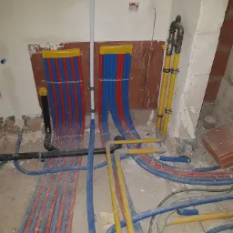 Instalacja ogrzewania podłogowego z rurami w kolorach niebieskim i czerwonym oraz żółte rury gazowe w surowym stanie, przed wylewką.