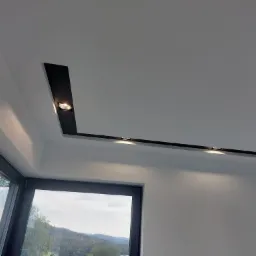 Nowoczesny sufit podwieszany z czarnymi wnękami i punktowym oświetleniem LED, widok z dołu na okno z widokiem na góry.