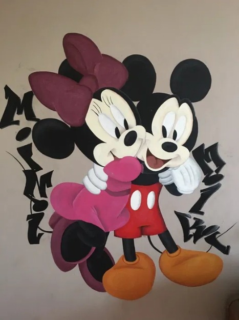 Mural przedstawiający przytulających się Myszki Miki i Minnie z napisem w stylu graffiti, wykonany farbami na beżowej ścianie.