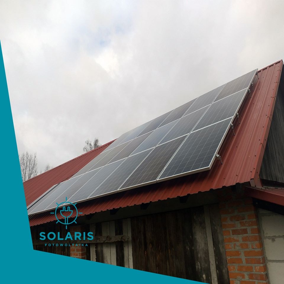 Panele słoneczne zamontowane na dachu budynku gospodarczego w Świdniku, widoczne mocowania na czerwonej blasze, pochmurne niebo w tle.