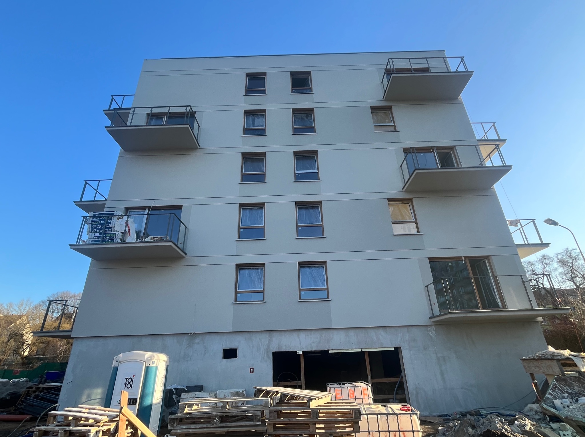 Nowoczesny budynek wielorodzinny z balkonami w Zielonej Górze, po wykonaniu elewacji. Widoczne rusztowania i materiały budowlane.