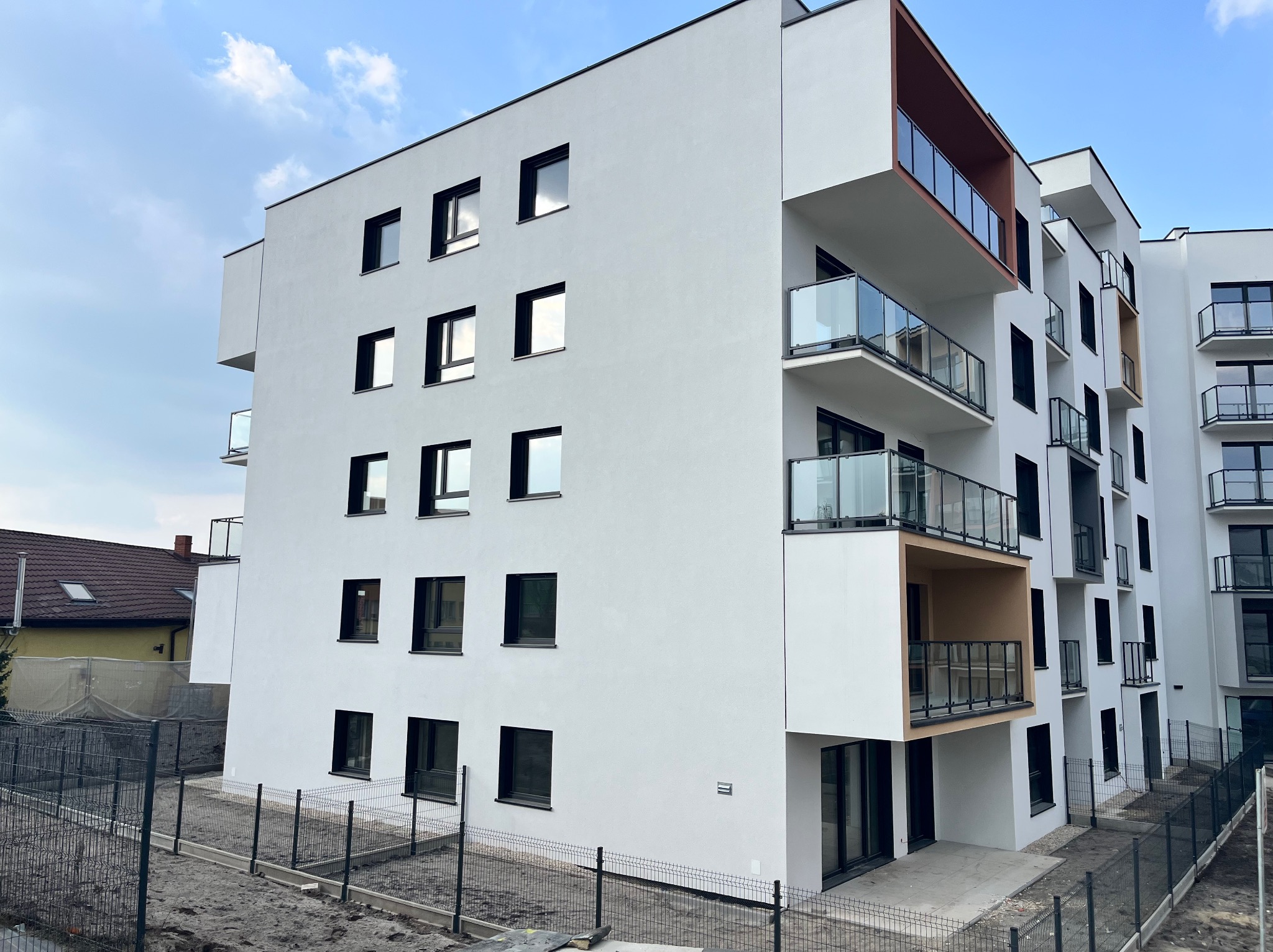 Nowoczesny budynek wielorodzinny z białymi elewacjami, czarnymi oknami i balkonami z szklanymi balustradami. Widok z dołu na budynek w słoneczny dzień.