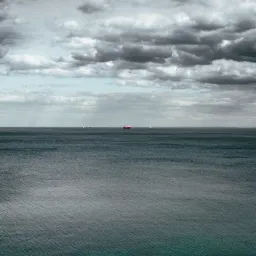 Odległy widok na morze z trzema statkami na horyzoncie pod pochmurnym niebem.