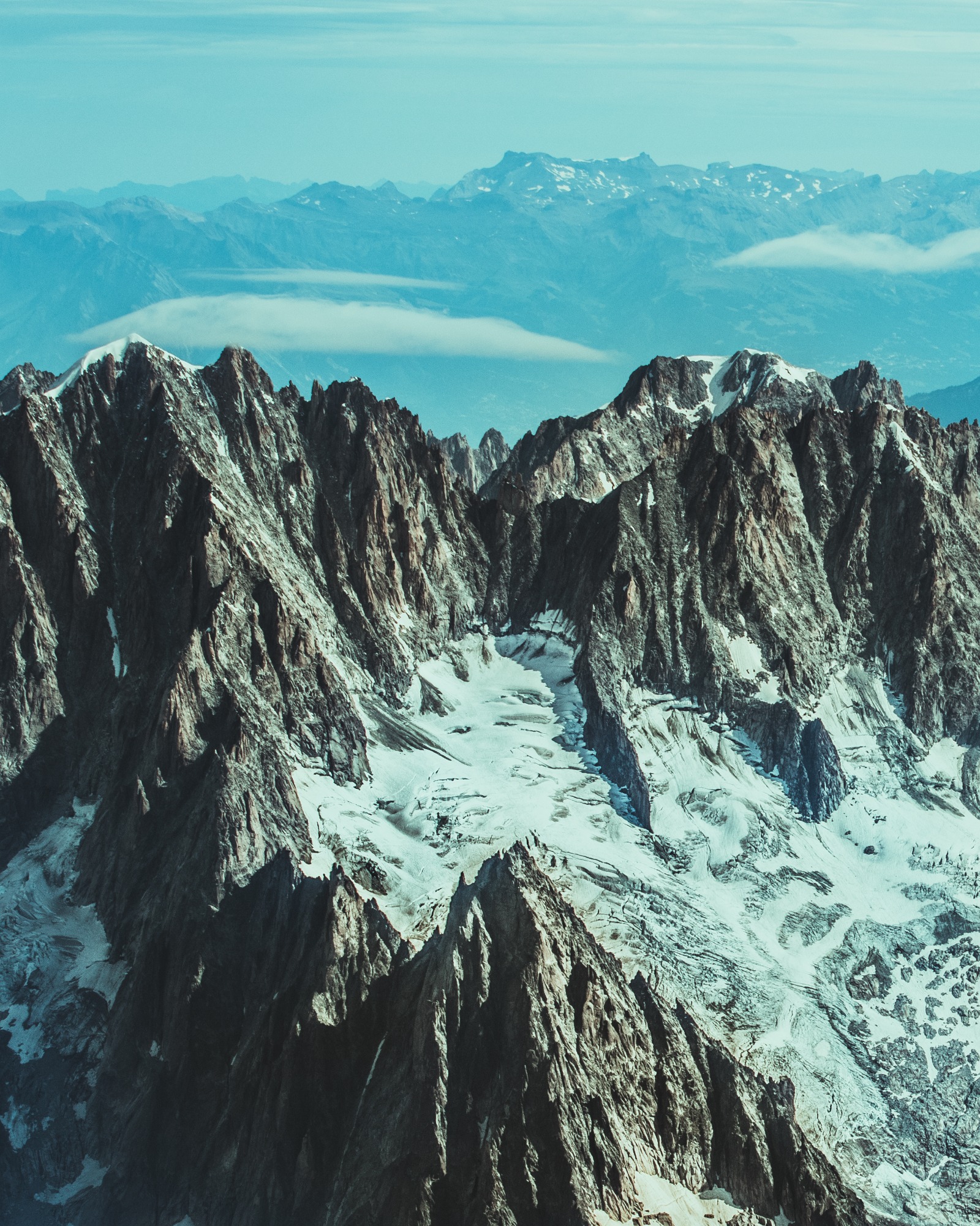 Szczyty górskie z resztkami śniegu i lodowca na zboczach, w tle kolejne pasma górskie spowite mgłą.