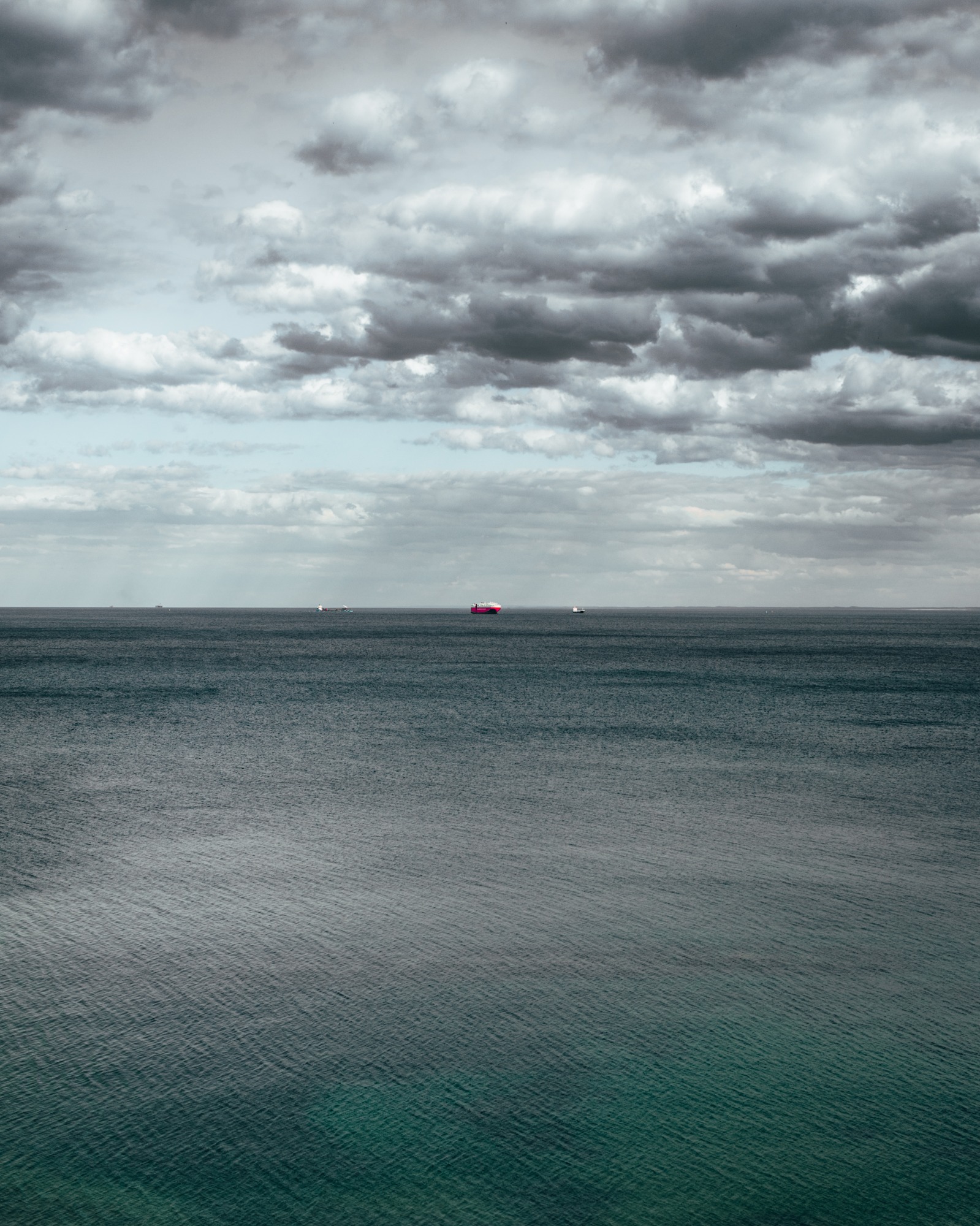 Odległy widok na morze z trzema statkami na horyzoncie pod pochmurnym niebem.