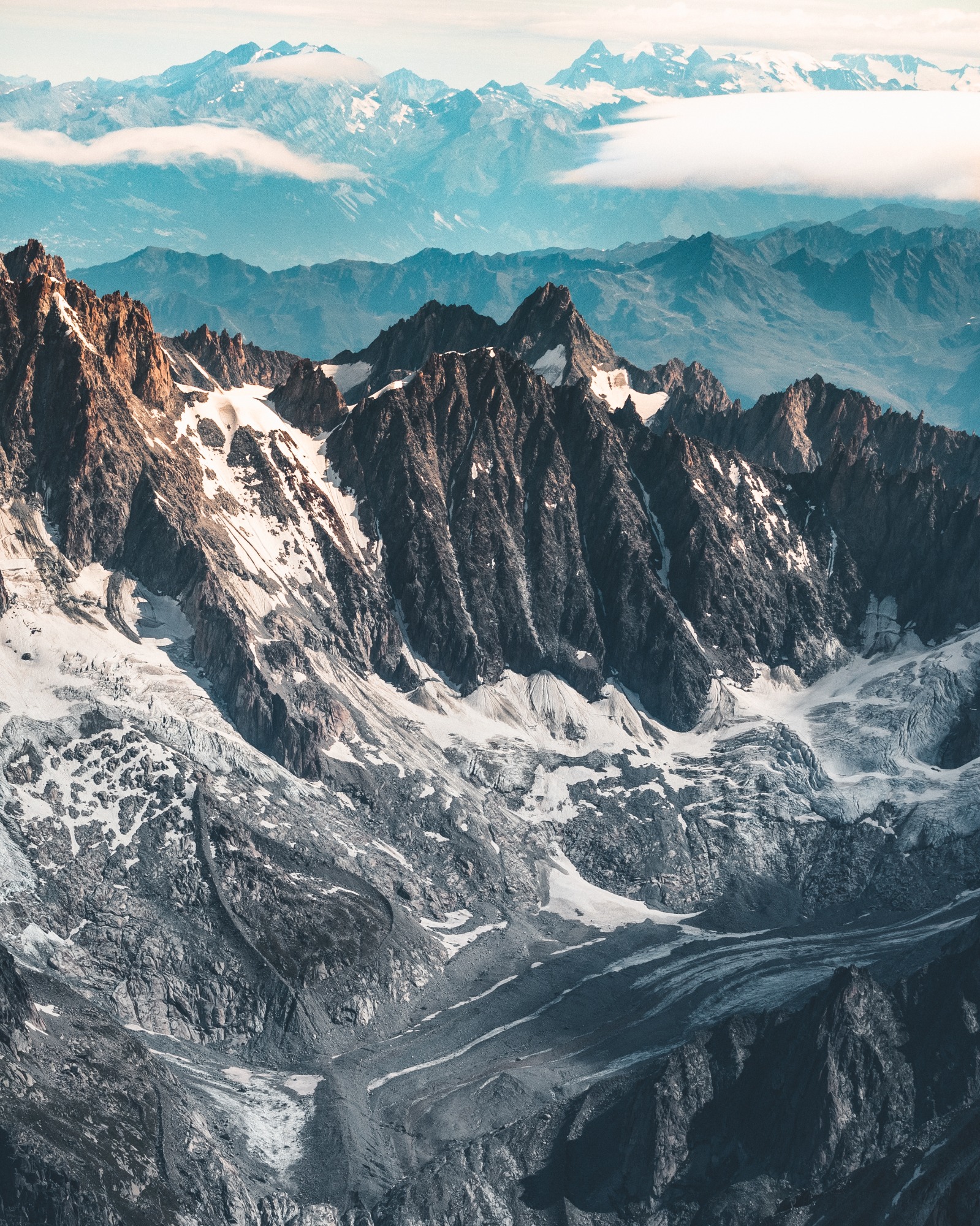Panoramiczny widok z lotu ptaka na ośnieżone szczyty górskie w słoneczny dzień, z odległymi szczytami spowitymi mgłą