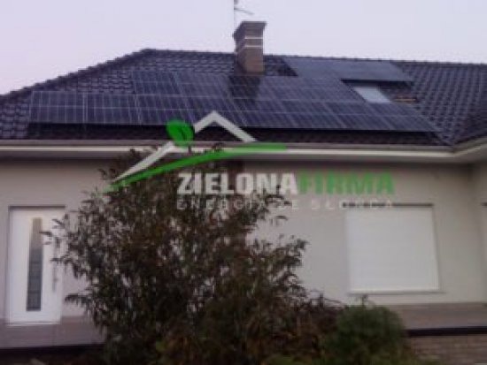 Dom jednorodzinny z panelami słonecznymi na dachu, widoczne logo firmy instalacyjnej na elewacji budynku.
