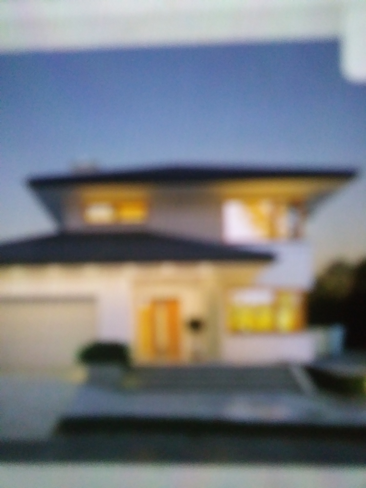 Rozmazane ujęcie dwupiętrowego domu z garażem, oświetlonego od wewnątrz, widzianego z zewnątrz o zmierzchu.