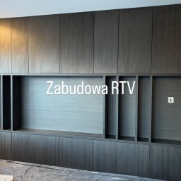 Mój.dom - Ciemna, drewniana zabudowa RTV z otwartymi półkami i szafkami, widoczna w trakcie montażu, z folią ochronną na podłodze. Minimalistyczny design.