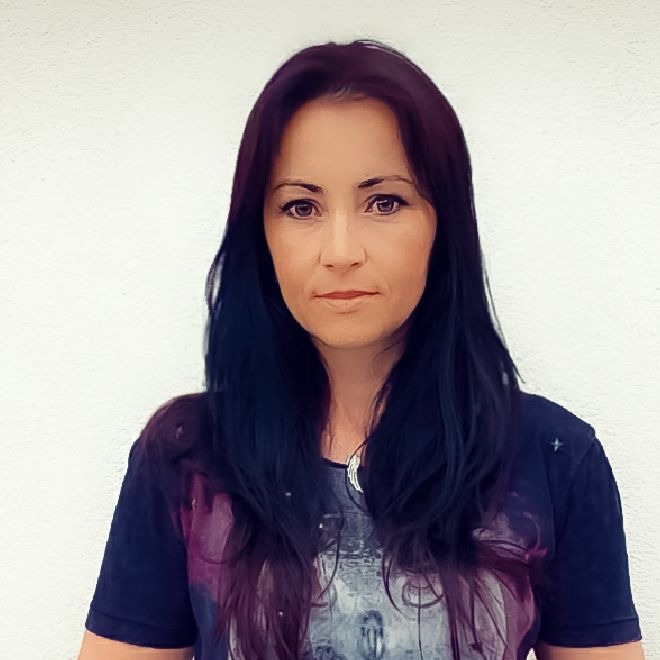 Portret kobiety z ciemnymi włosami i delikatnym makijażem, na tle jasnej ściany.