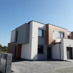 Nowoczesny, dwukondygnacyjny dom bliźniak z elewacją w odcieniach bieli, szarości i drewna, z widocznymi kamerami monitoringu i kostką brukową przed wejściem, sfotografowany w słoneczny dzień.