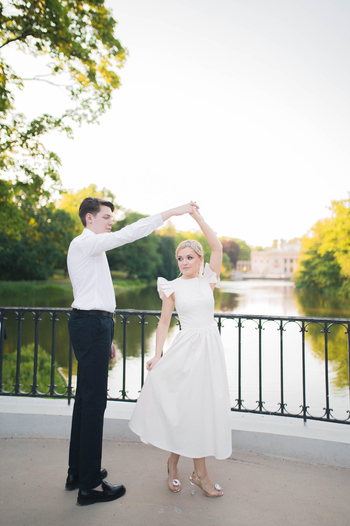 Para młoda w tańcu na moście w Łazienkach Królewskich, Pałac na Wodzie w tle, panna młoda w sukni z bufkami i zdobnych sandałach na obcasie.