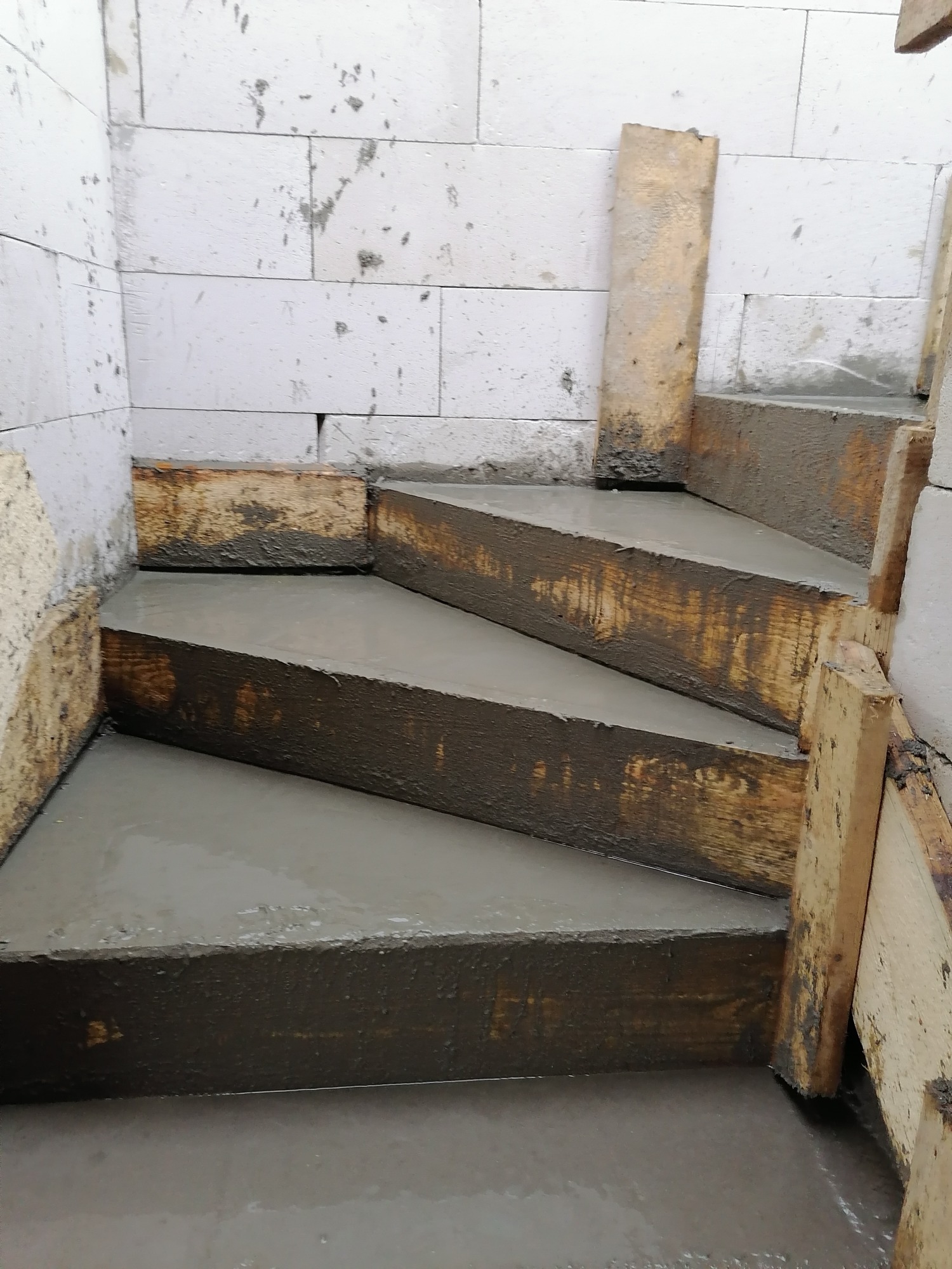 Wylewanie betonowych schodów wewnątrz budynku z bloczków betonowych, widoczne drewniane szalunki.
