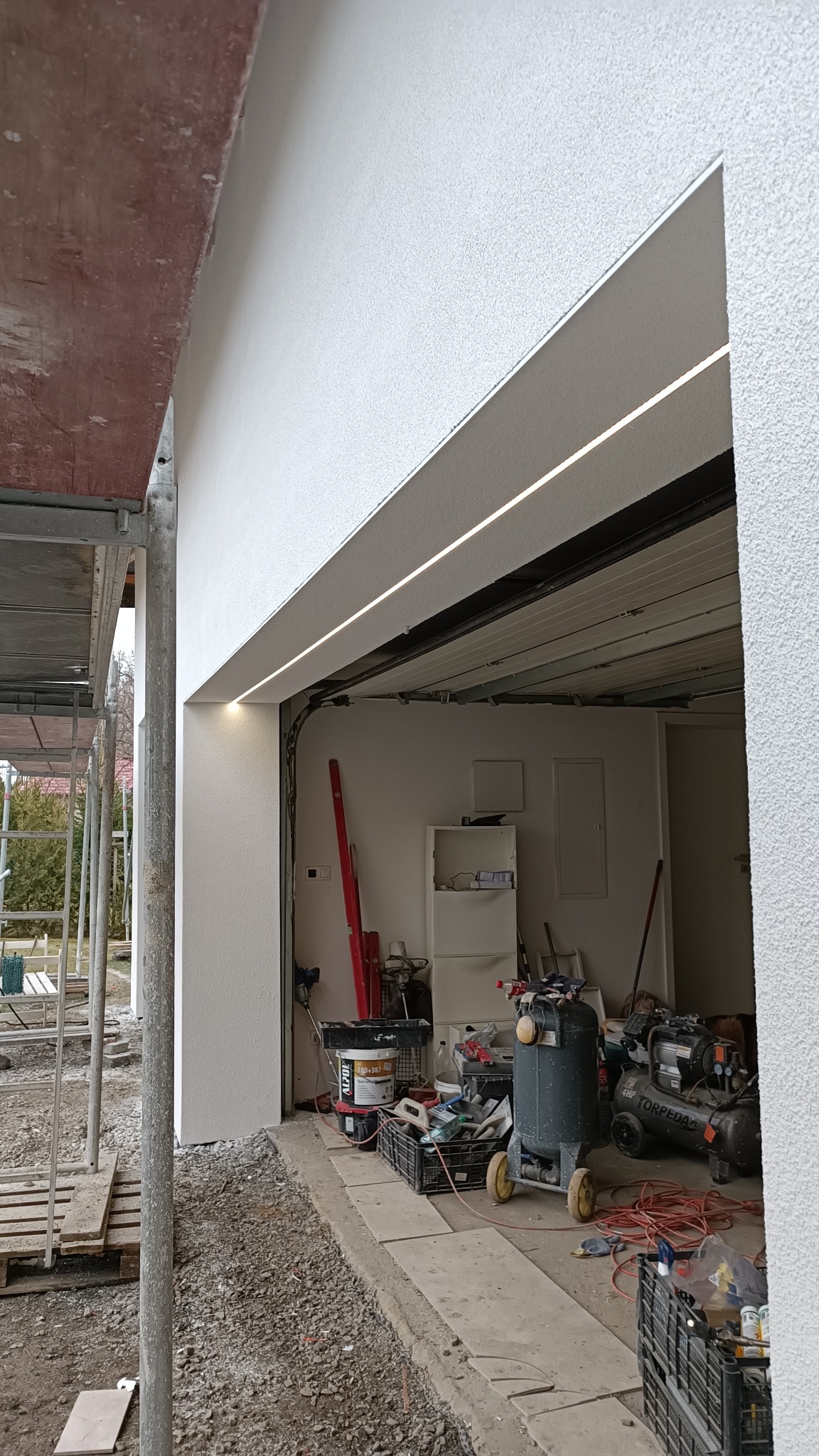 Świeżo otynkowana elewacja garażu w Wodzisławiu Śląskim, widoczne narzędzia i kompresory wewnątrz, fragment rusztowania z lewej strony.