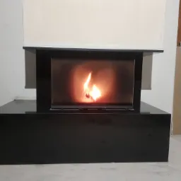 Nowoczesny czarny kominek z płomieniem w trakcie montażu, widoczne niedokończone ściany i podłoga.