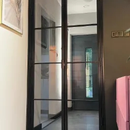 Dwuskrzydłowe drzwi wewnętrzne z czarną metalową ramą i szprosami, widoczne wnętrze z szarą podłogą i ciemnymi drzwiami w tle.