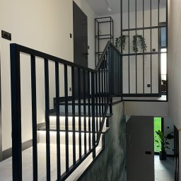 G-Weld - Nowoczesne schody z podświetlanymi stopniami i czarną, minimalistyczną balustradą, widok z góry na dół, z elementami dekoracyjnymi jak rośliny wiszące i półka w tle.