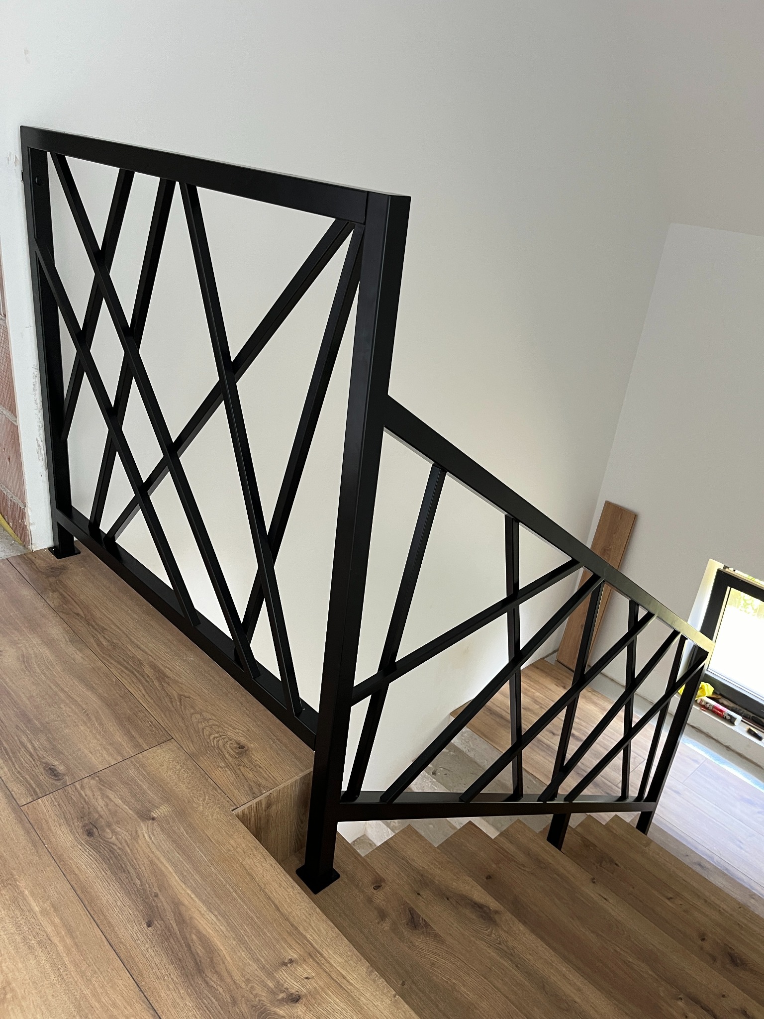 Nowoczesna, czarna barierka schodowa z geometrycznym wzorem, zamontowana na schodach wykończonych panelami imitującymi drewno, widok z góry.