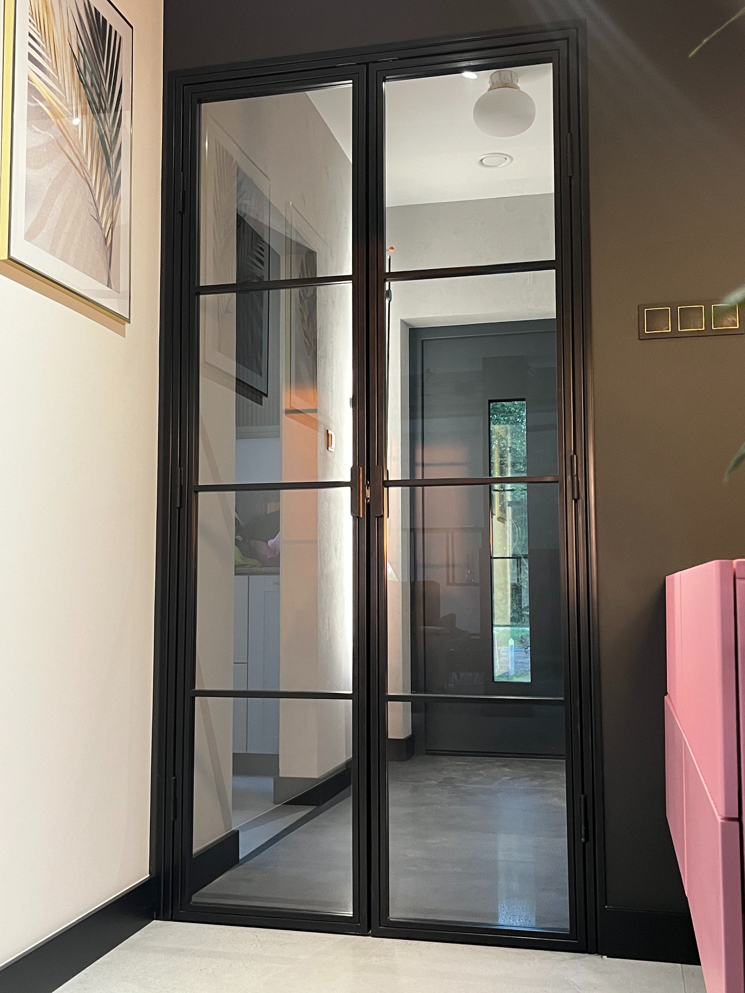 Dwuskrzydłowe drzwi wewnętrzne z czarną metalową ramą i szprosami, widoczne wnętrze z szarą podłogą i ciemnymi drzwiami w tle.