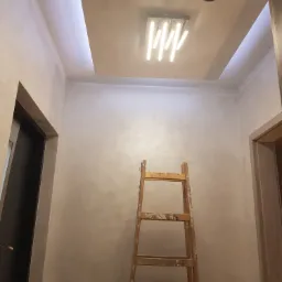 Montaż oświetlenia w suficie podwieszanym z płyty karton gips, widoczna drewniana drabina i ściany wykończone gładzią.
