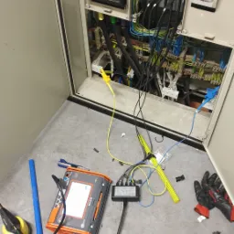 Otwarta szafa elektryczna z widocznymi przewodami i zabezpieczeniami, obok leżą narzędzia: miernik wielofunkcyjny MPL-S40 z podłączonym modułem, kombinerki, wkrętak i wiertarka akumulatorowa.