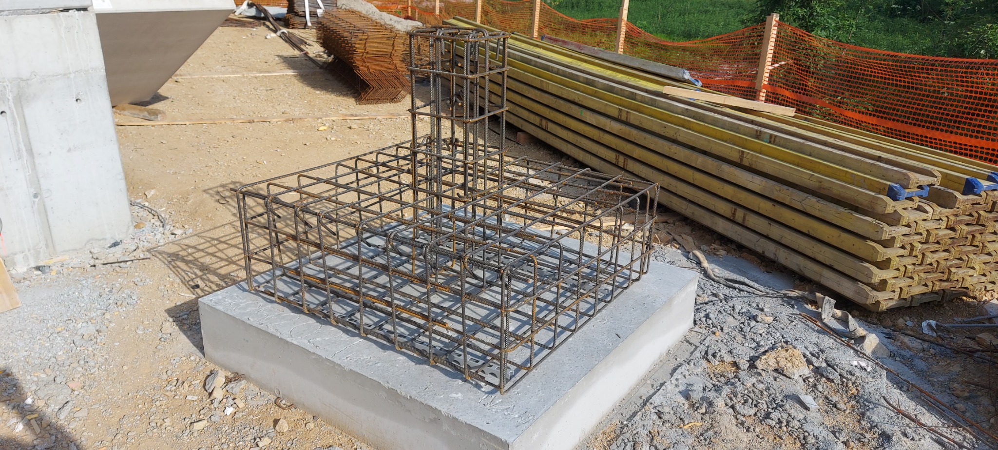 Zbrojenie fundamentu na betonowej podstawie, widoczne deski szalunkowe i siatka zabezpieczająca w tle.