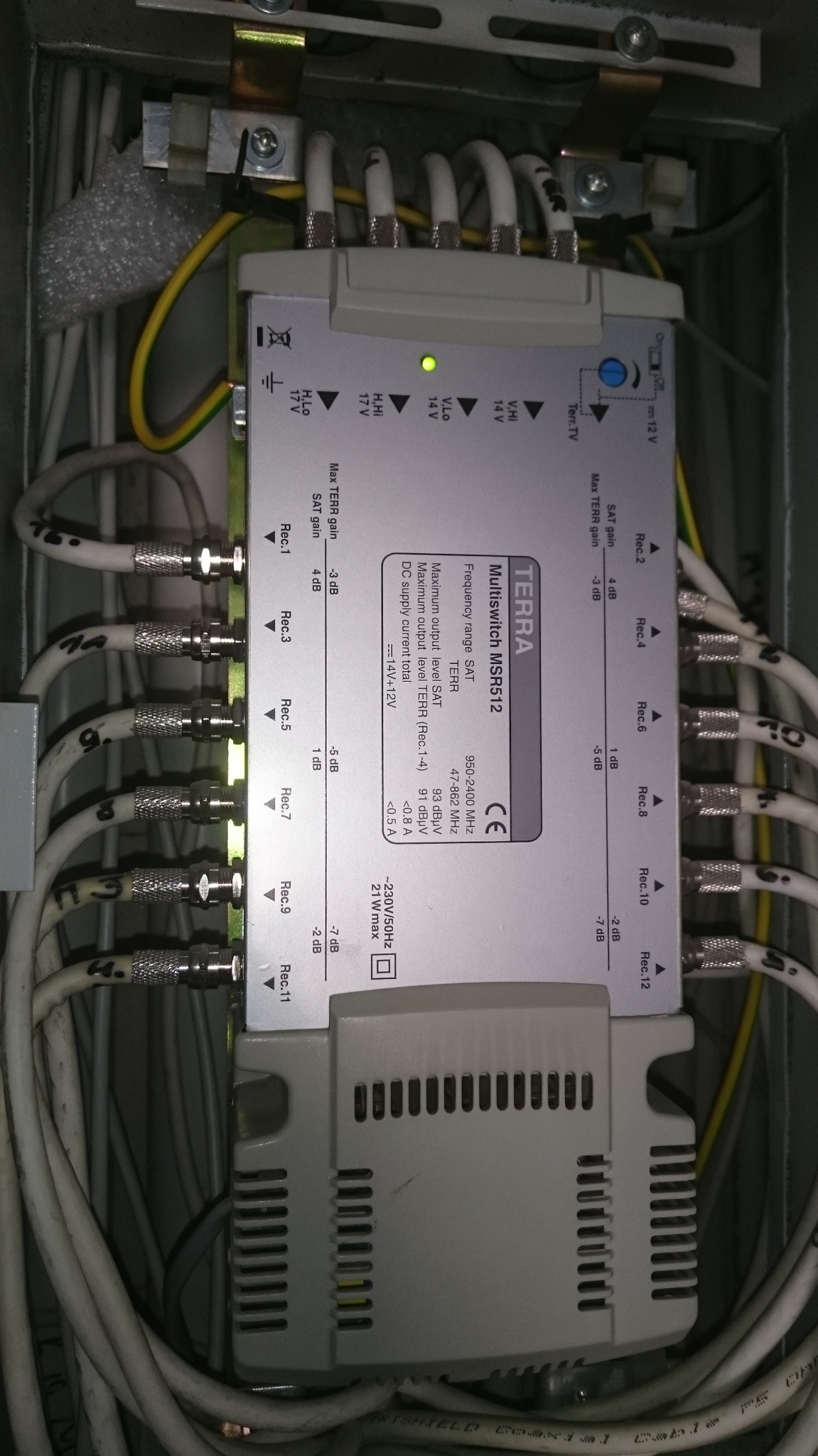 Multiswitch Terra MSR512 w metalowej obudowie z podłączonymi kablami koncentrycznymi, widoczne oznaczenia portów Rec.1 do Rec.12 oraz zasilanie 230V, zielona dioda LED sygnalizuje pracę.