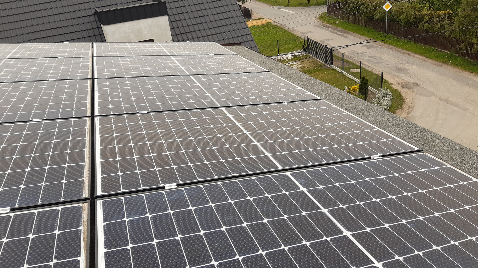 Panel słoneczny na dachu domu jednorodzinnego z widokiem na ulicę i znak drogowy.