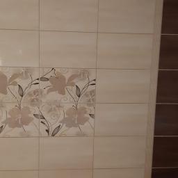 Lilbud Project - Ściana wyłożona beżowymi i brązowymi płytkami ceramicznymi z motywem kwiatowym, widoczne dwa chromowane zawory.