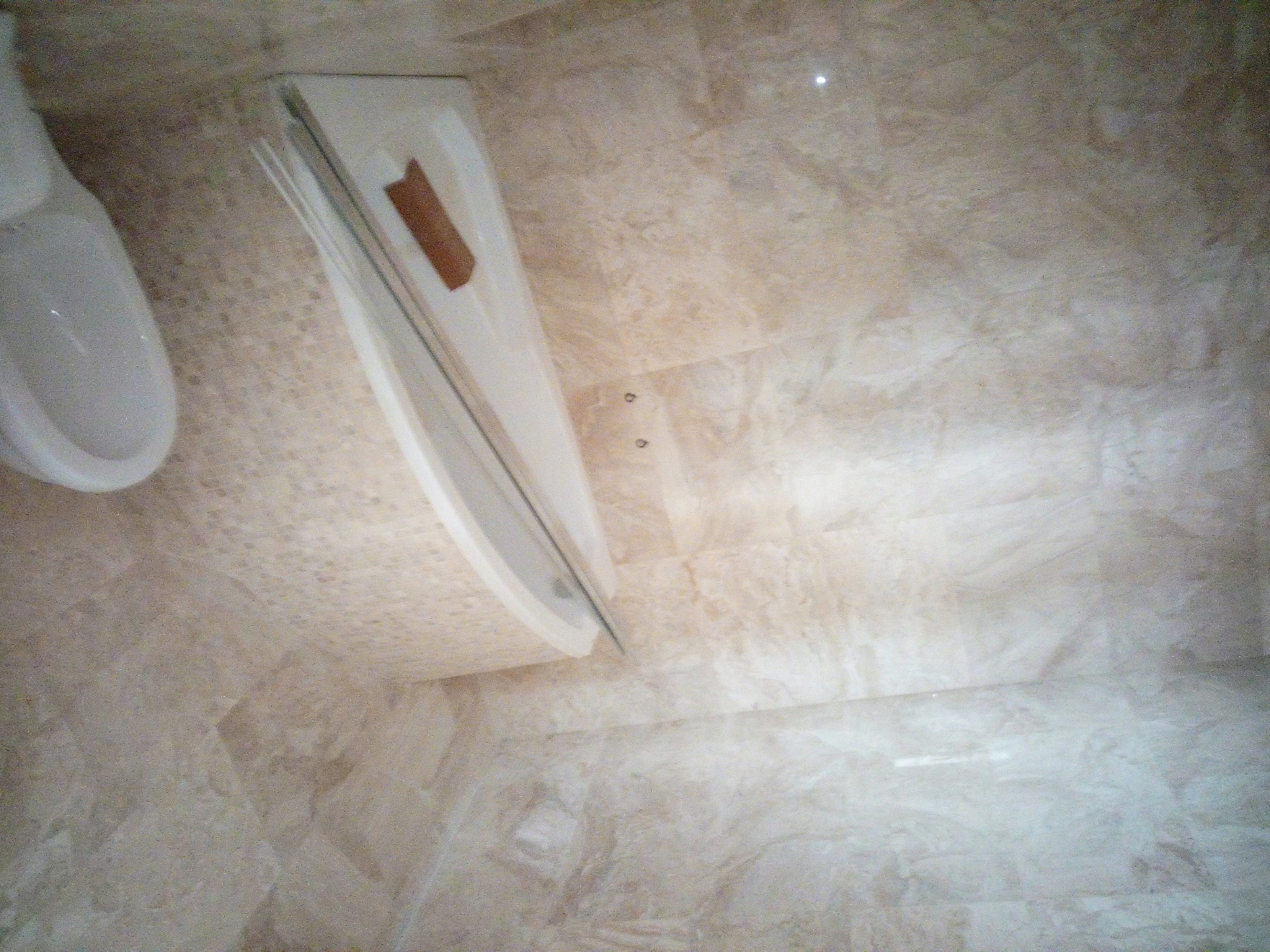 Wykończona łazienka z beżowymi płytkami imitującymi marmur, widoczna umywalka i kabina prysznicowa z przezroczystym szkłem, zamontowana na ścianie.