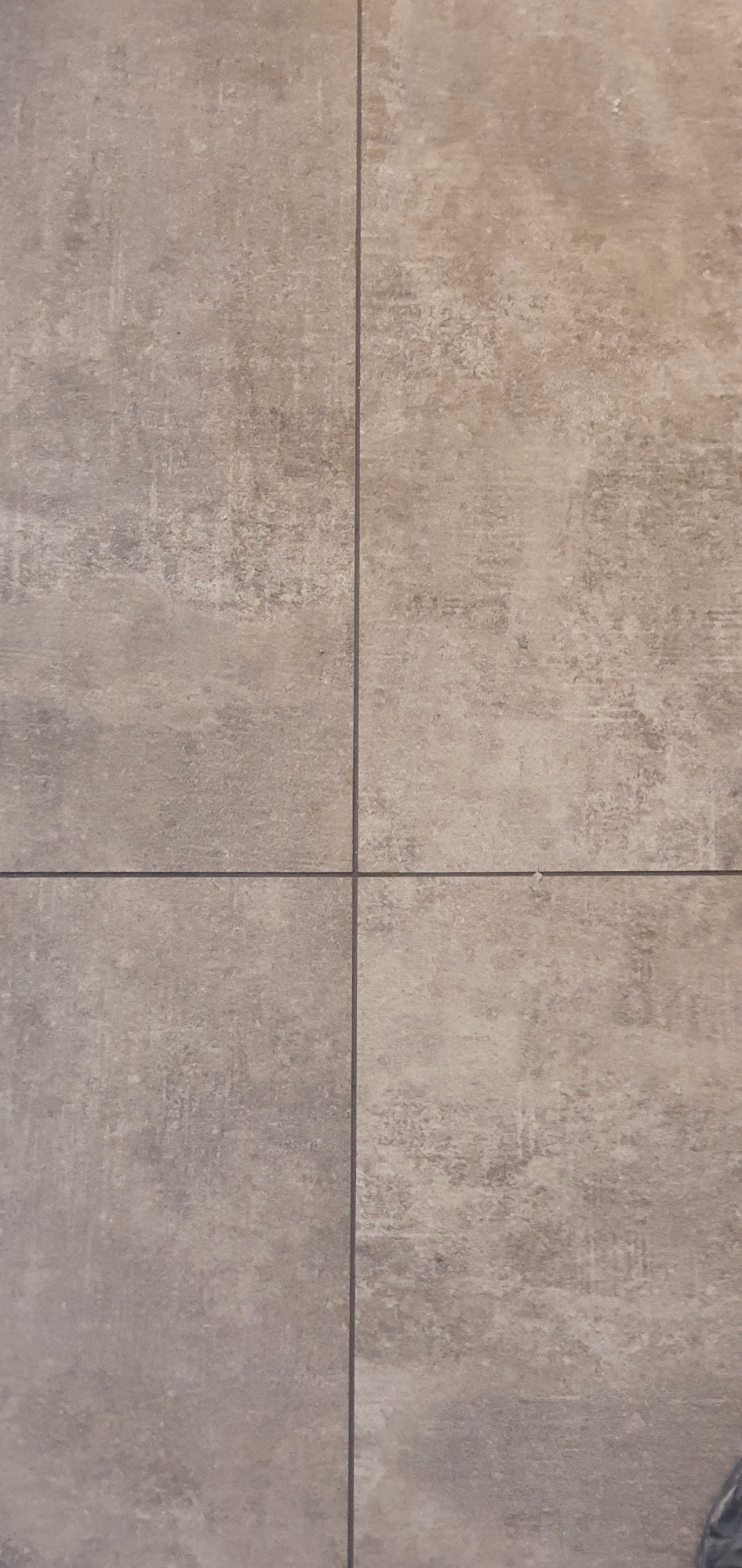 Beżowe, matowe płytki podłogowe ułożone w kwadraty z ciemnymi fugami, imitujące betonową powierzchnię.
