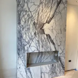 Ściana z białego marmuru z szarymi żyłami, w której wkomponowano wnękę, widoczne niedokończone wykończenia ścian i podłogi.