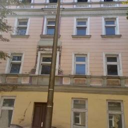 Molbud - Elewacja kamienicy przed remontem, widoczne okna z drewnianą stolarką, ślady po pożarze na górnych oknach, stara lampa uliczna i dwie osoby na pierwszym planie