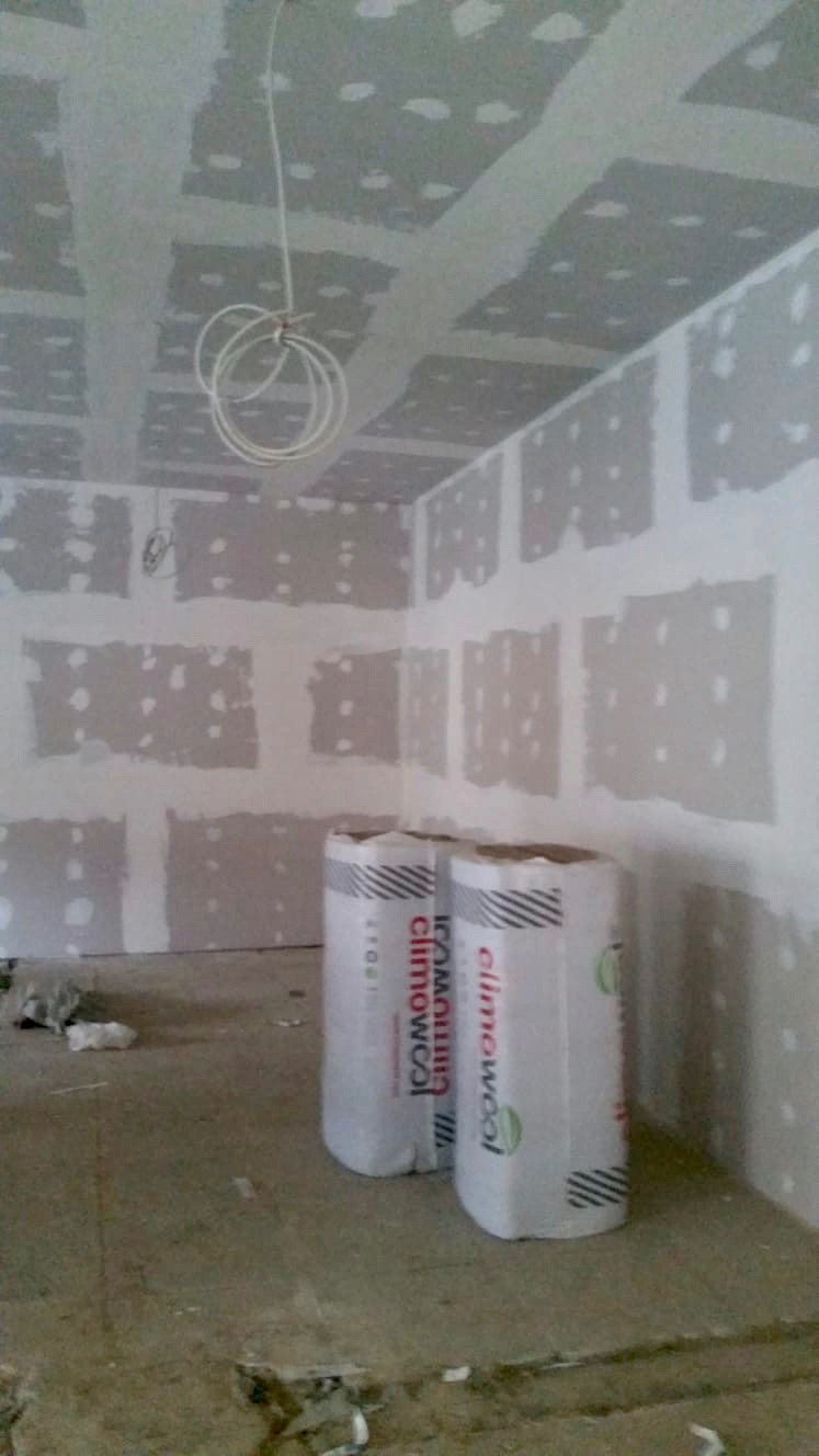 Wnętrze w trakcie prac wykończeniowych: widoczne płyty kartonowo-gipsowe na ścianach i suficie, częściowo zaszpachlowane, z dwoma rolkami wełny mineralnej Climowool na podłodze i zwisającym kablem...