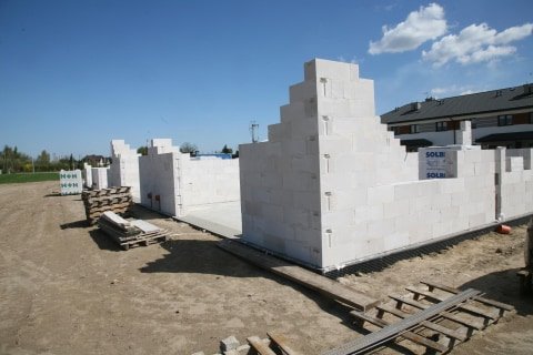 Wznoszenie ścian parteru domu z bloczków betonu komórkowego Solbet, widoczne palety z materiałem i podłoże przygotowane pod dalszą budowę.