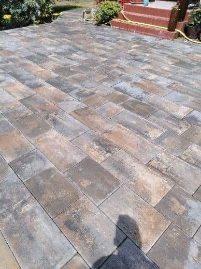 Ułożona kostka brukowa w odcieniach szarości, brązu i beżu, ułożona w jodełkę, widoczne schody z czerwonej cegły i zieleń w tle.