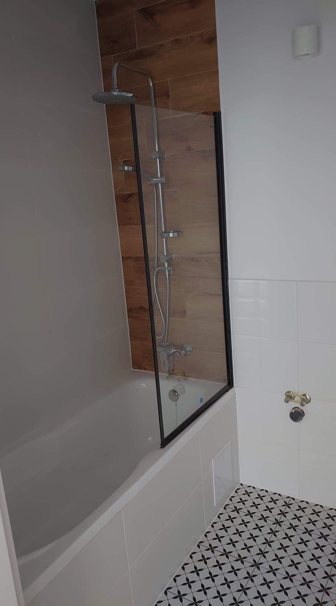 Nowoczesna łazienka z wanną i szklanym parawanem, drewnopodobne panele na ścianie, czarno-biała mozaika na podłodze.