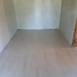 Pokój po szpachlowaniu ścian i wylewce podłogi, widoczny drewniany słup konstrukcyjny w tle.