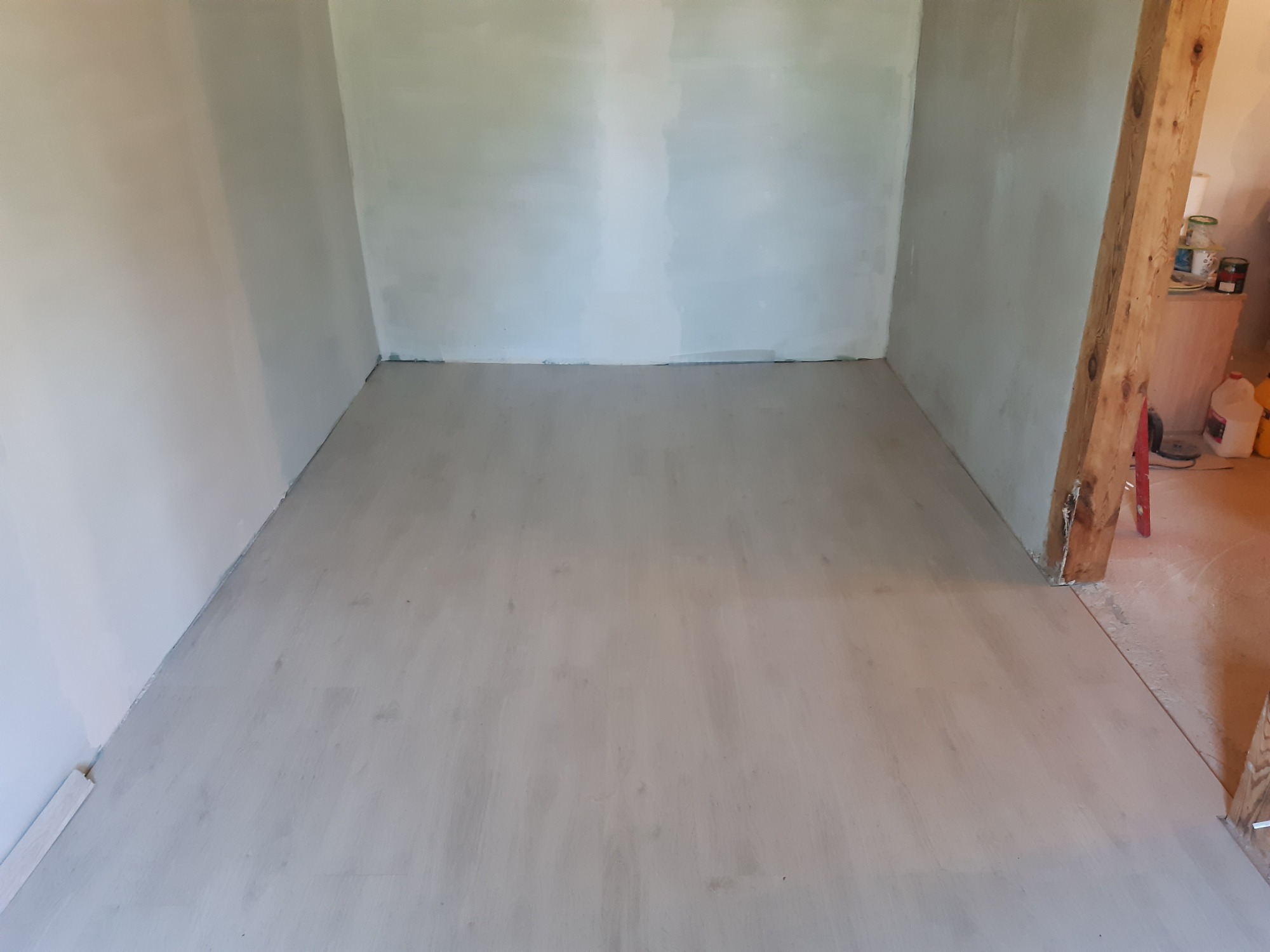 Pokój po szpachlowaniu ścian i wylewce podłogi, widoczny drewniany słup konstrukcyjny w tle.