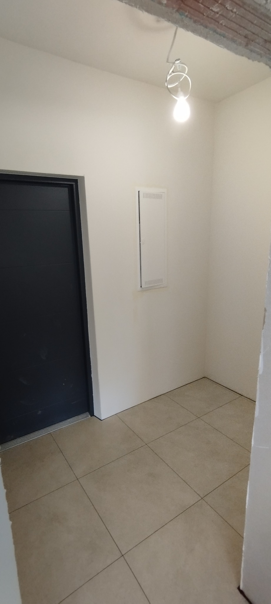 Wnętrze po remoncie: świeżo pomalowane ściany na biało, ciemne drzwi, beżowe płytki podłogowe, widoczna instalacja elektryczna pod sufitem.