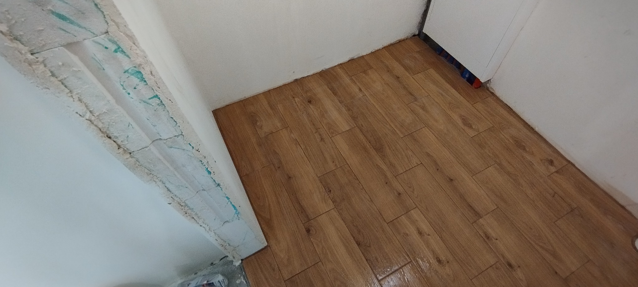 Ukończone układanie paneli podłogowych w pomieszczeniu, widoczne świeżo położone panele, ściana z widocznymi śladami po remoncie i gładzi.