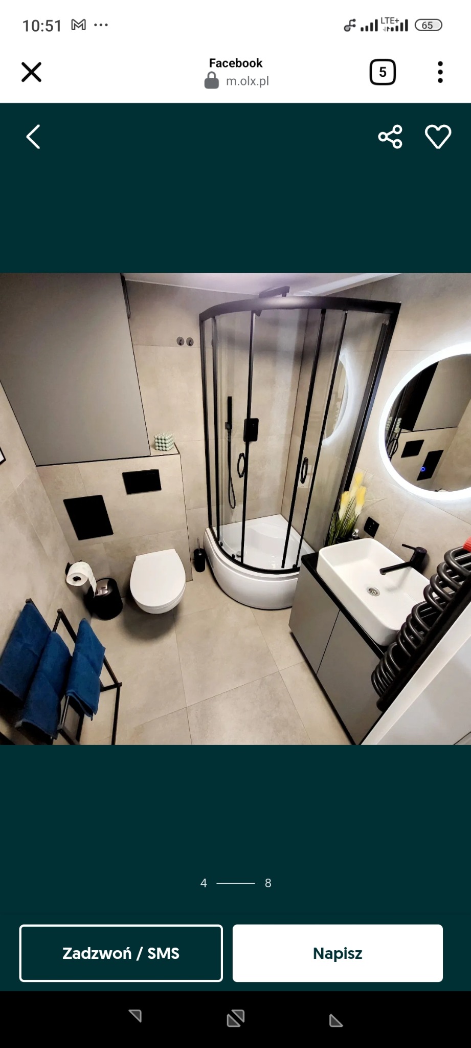 Nowoczesna łazienka z kabiną prysznicową z czarnymi ramami, umywalką na szafce, podświetlanym lustrem i beżowymi płytkami. Minimalistyczny design.