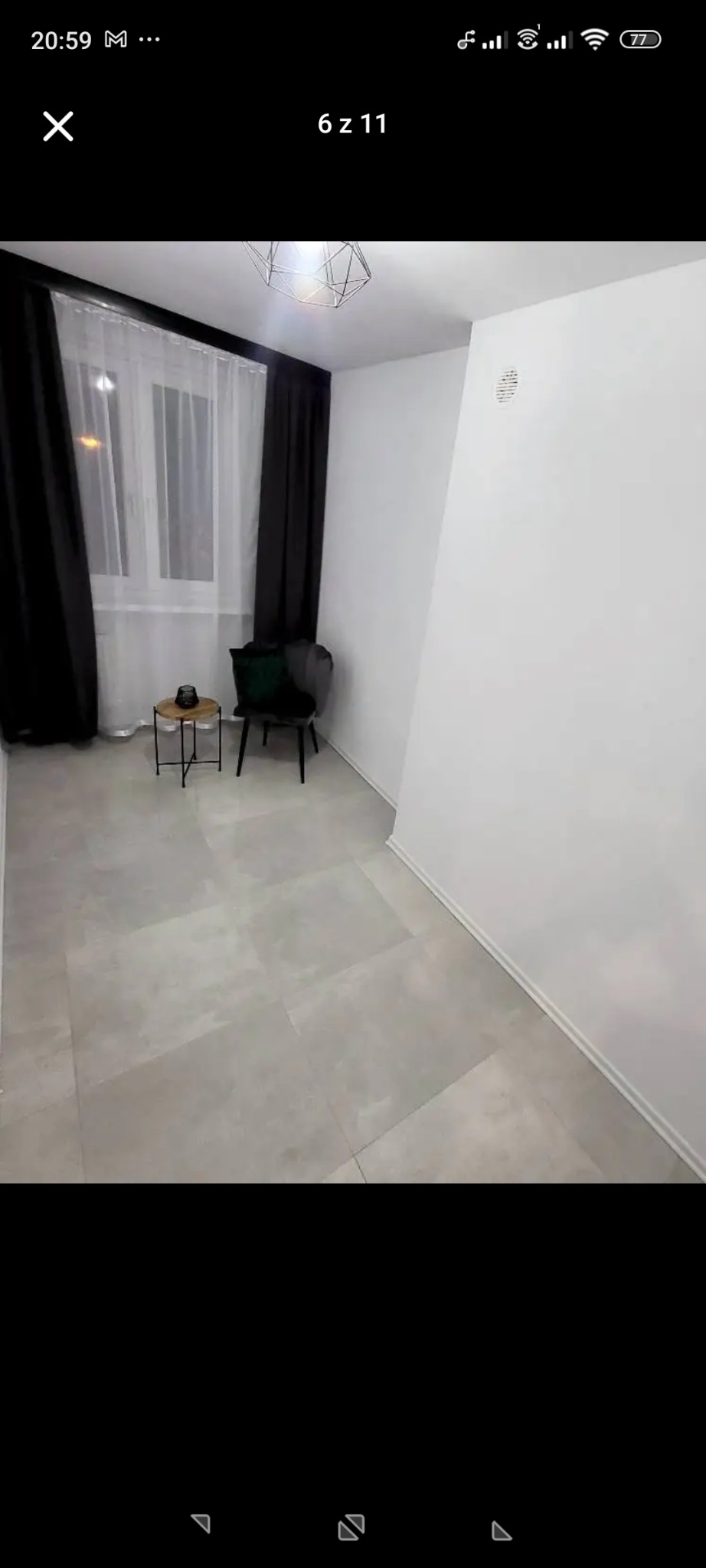 Wykończone wnętrze pokoju z szarymi płytkami podłogowymi, białymi ścianami i czarnymi zasłonami. Nowoczesna lampa sufitowa i minimalistyczny stolik kawowy.